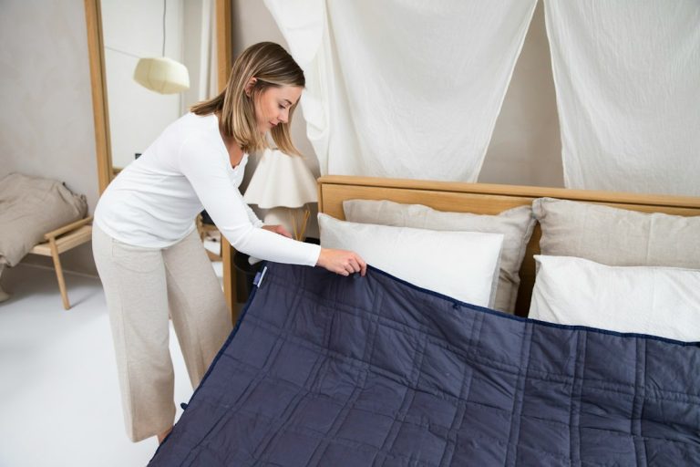 A woman preparing her property for the summer rental season, making a bed with white sheets and a blue over blanket