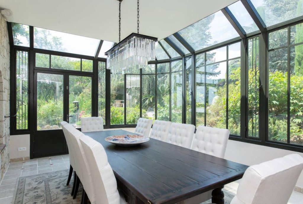 A dark wooden table surrounded by white upholstered chairs in an light and airy garden room/conservatory at Villa Eucalyptus on the French Riviera